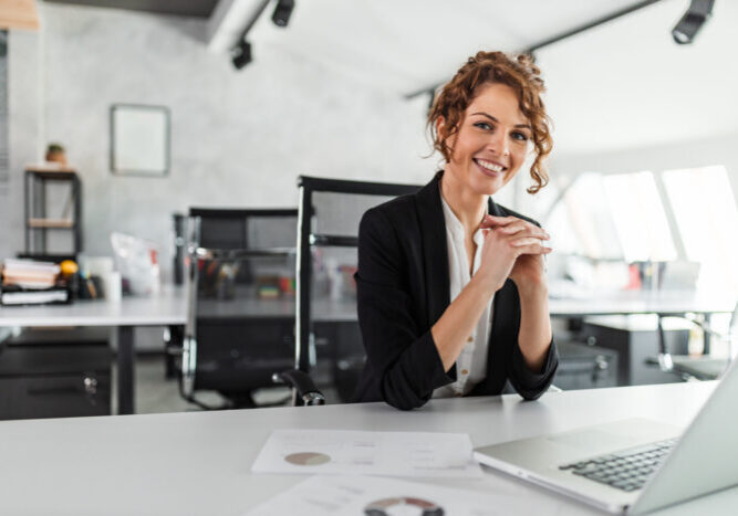 Portrait of a happy manager at bright office. Smiling at camera while sitting at office desk.